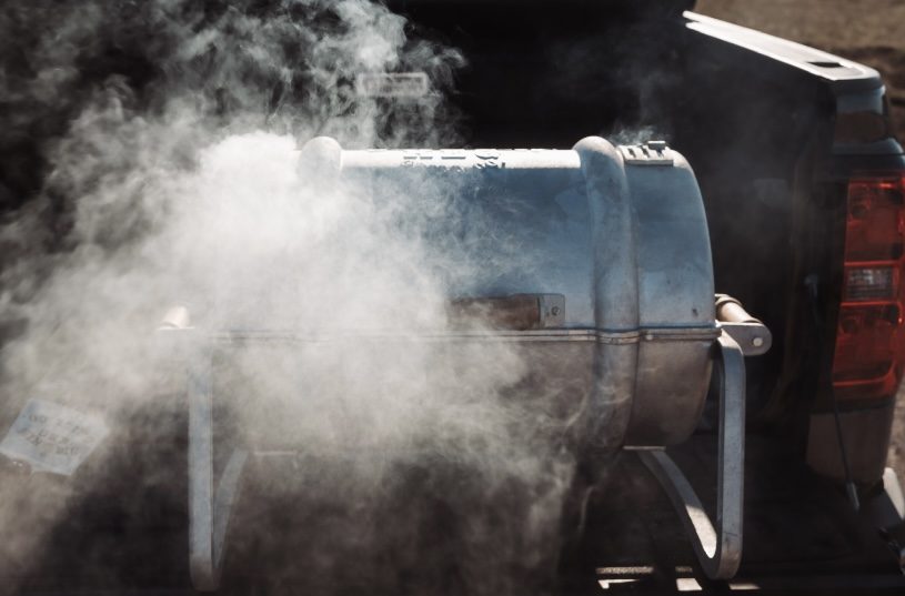 Smoke rolling out of a closed Smokin' Keg grill on a tailgate
