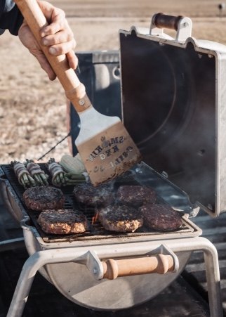 Burgers on the grate with a Smokin' Keg branded spatula