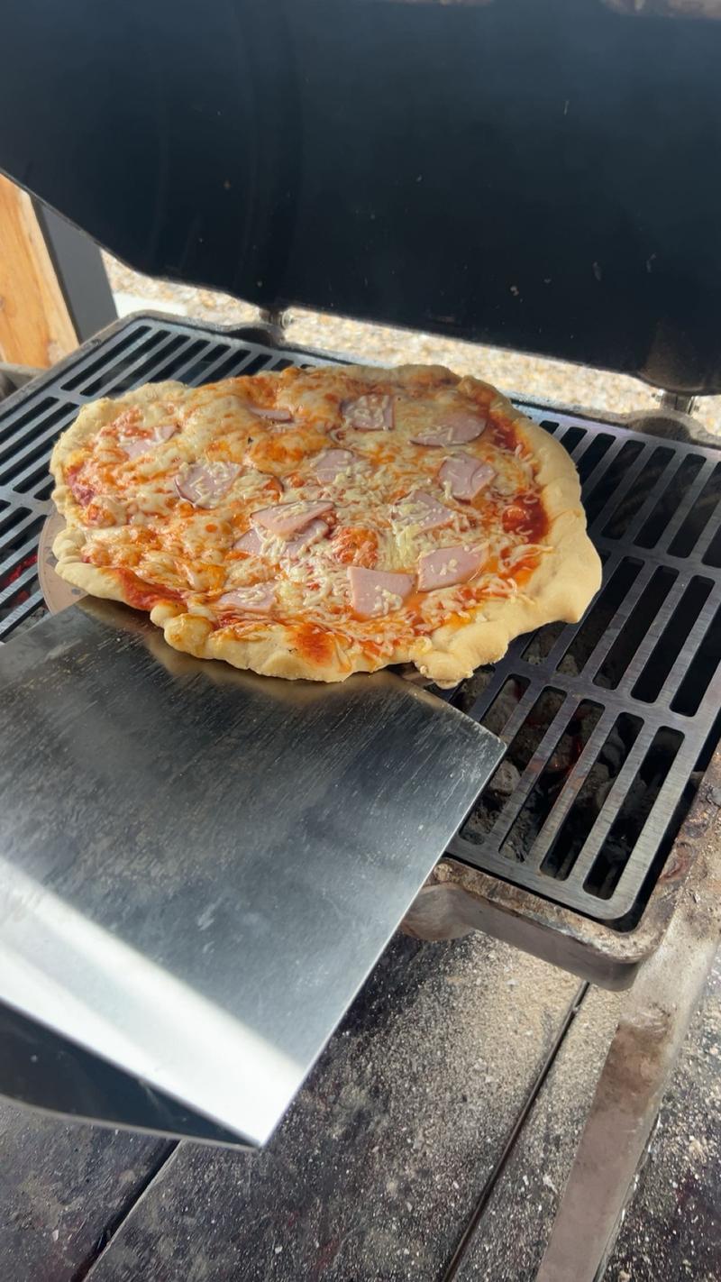 A pizza cooking on the grate of a Smokin' Keg grill