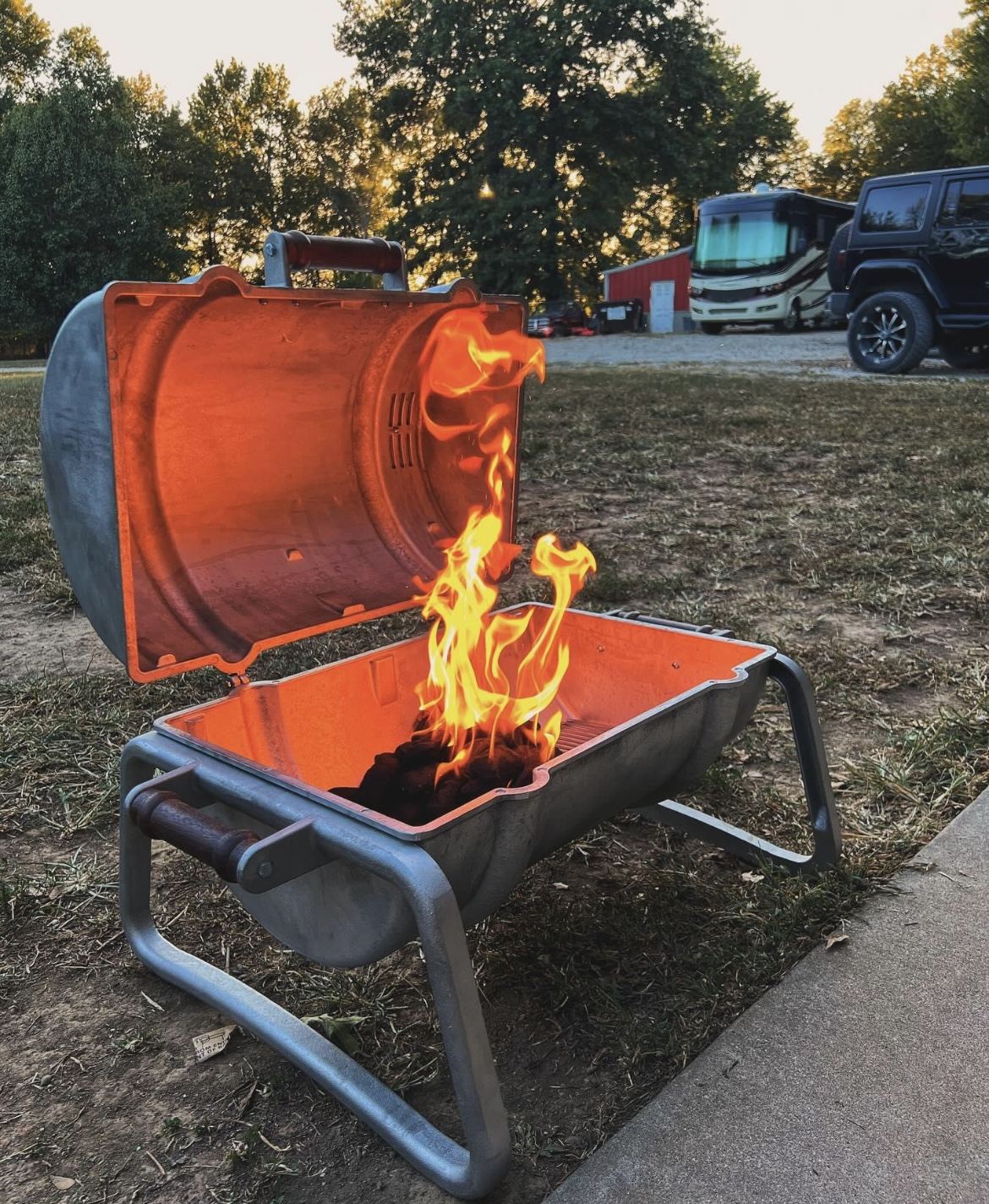 A Smokin' Keg grill running open flame at a campsite at dusk